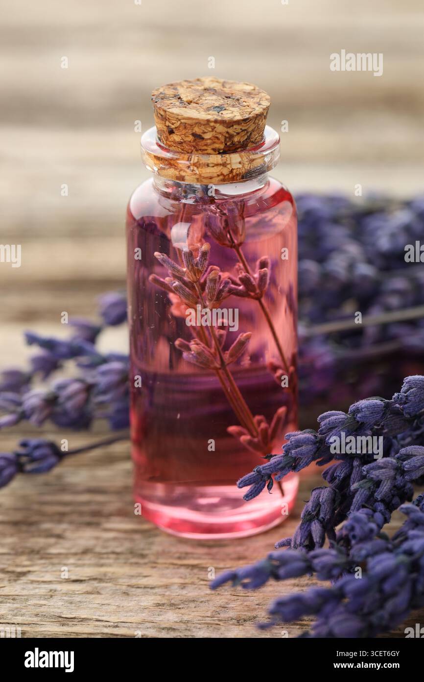 Olio essenziale di lavanda in bottiglia e fiori su tavola di legno, primo piano Foto Stock