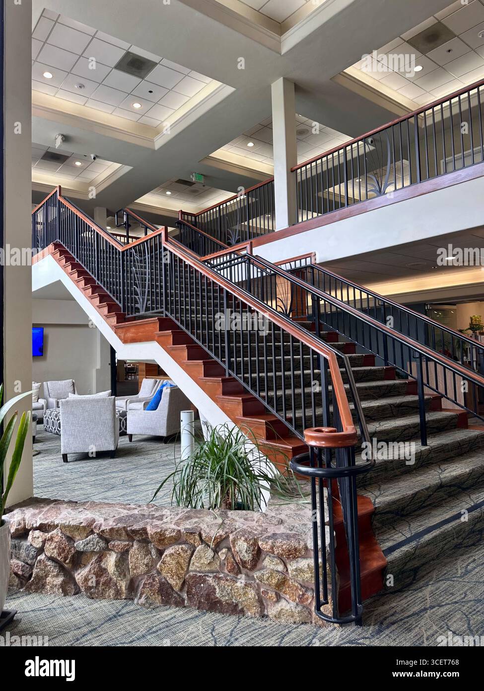 Scala in legno e tappeto con ringhiere nere e base in pietra all'interno di un moderno edificio interno con area lounge. - Immagine stock catturata con smartphone