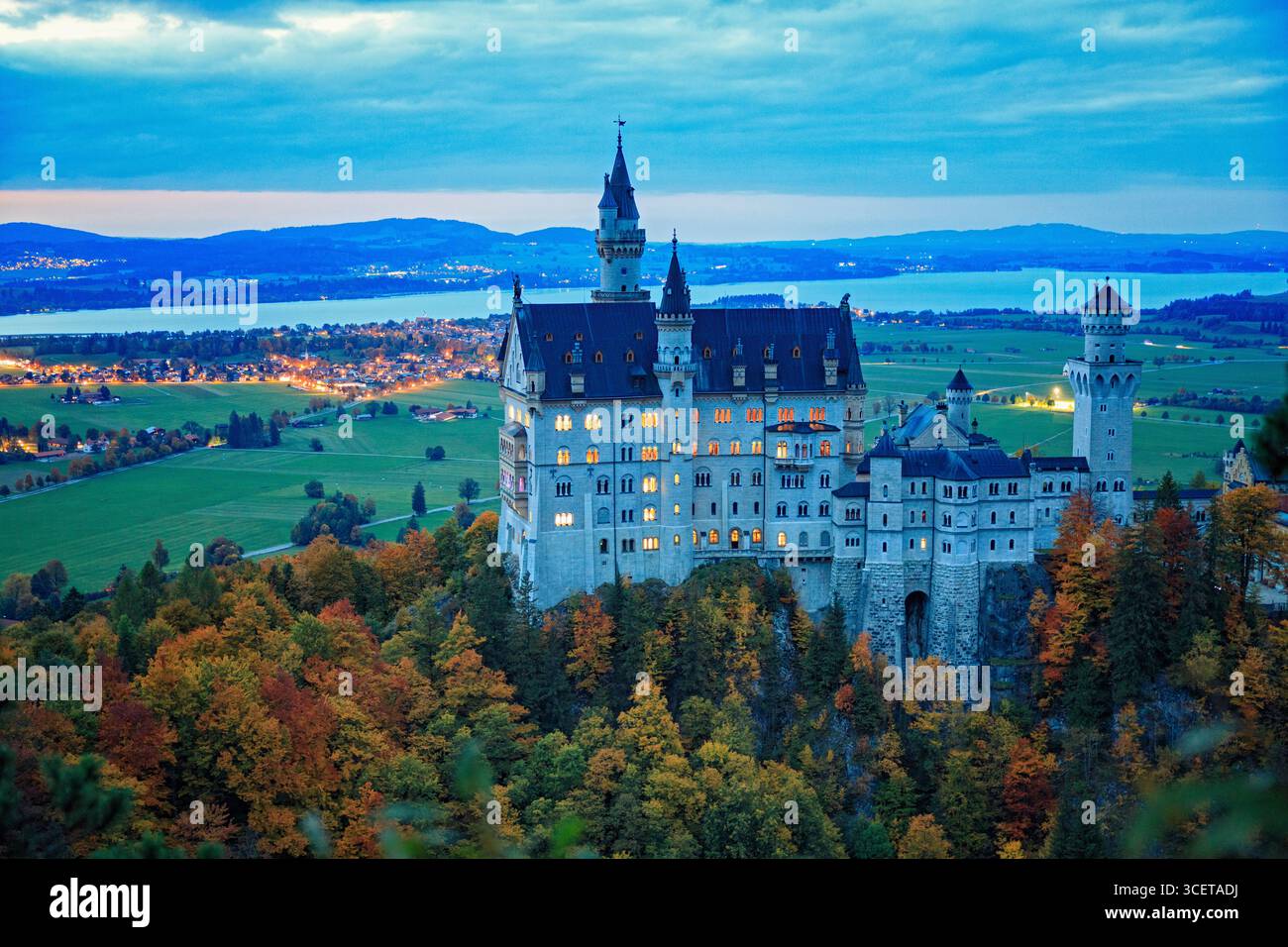 Schwangau, Germania - 6 ottobre 2022: Castello di Neuschwanstein illuminato al crepuscolo con finestre luminose e foresta autunnale in Baviera. Foto Stock