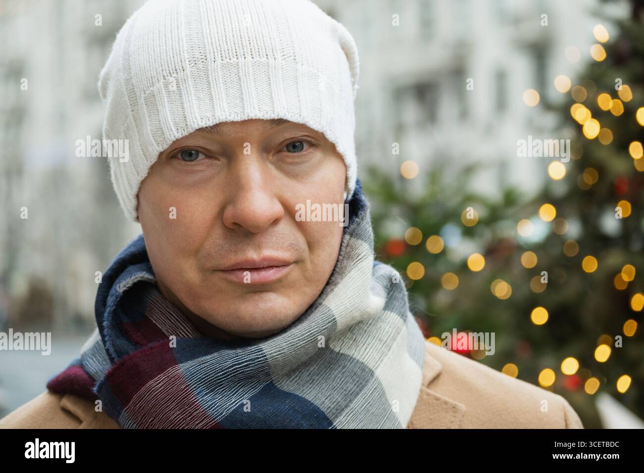 Ritratto di un uomo che indossa un berretto bianco e un'accogliente sciarpa, con sfondo sfocato per le festività natalizie. Clima invernale freddo. Foto Stock