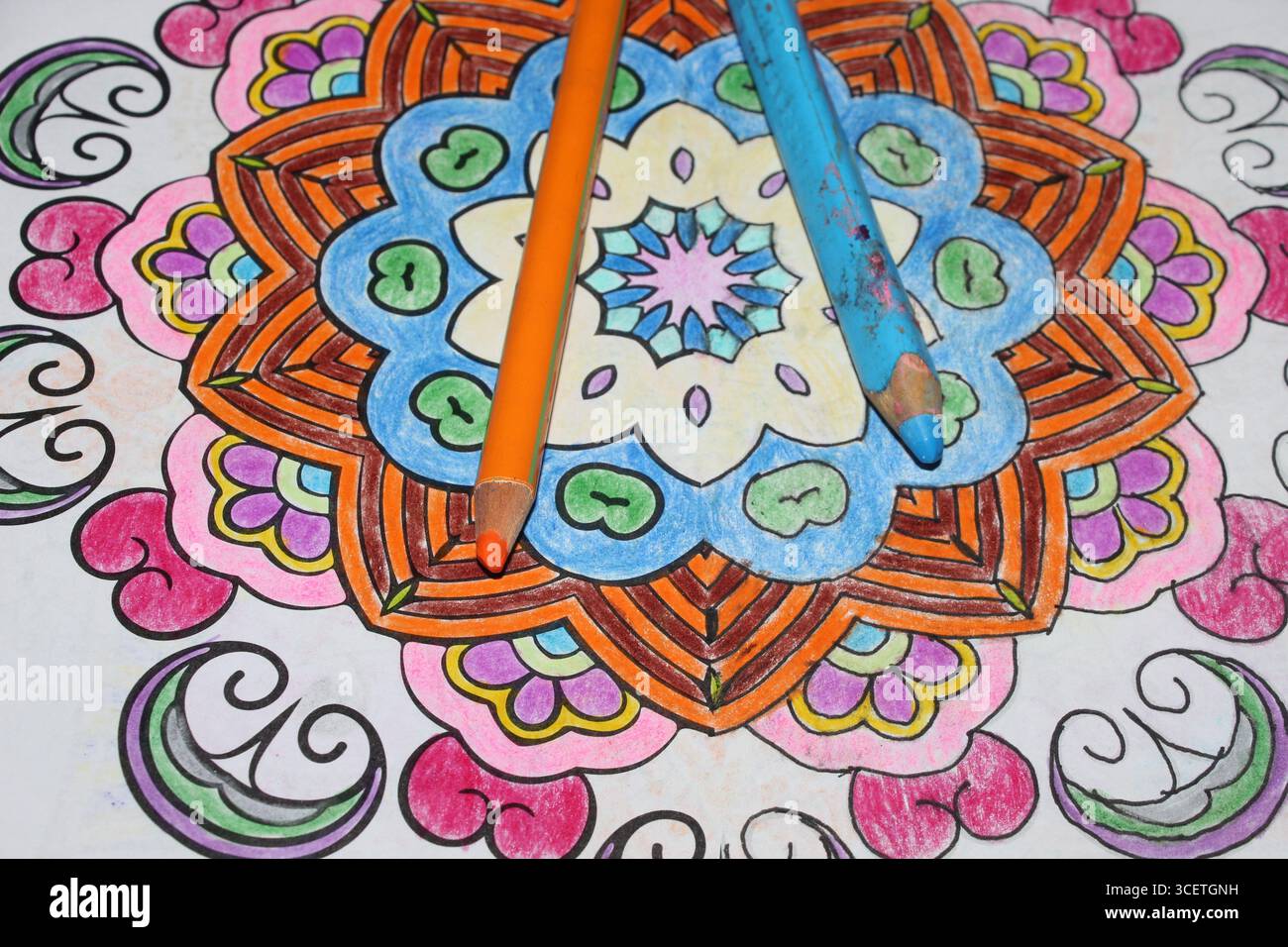 Matita di colore blu e arancione adagiata su un disegno di mandala colorato Foto Stock