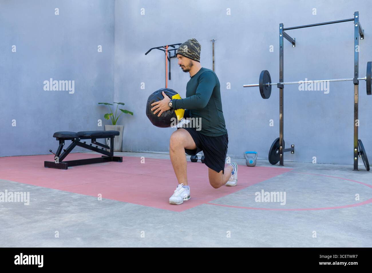 L'atleta esegue affondi mentre si afferra una palla medica in una palestra all'aperto, dimostrando forza ed equilibrio durante una sessione di allenamento intensa Foto Stock