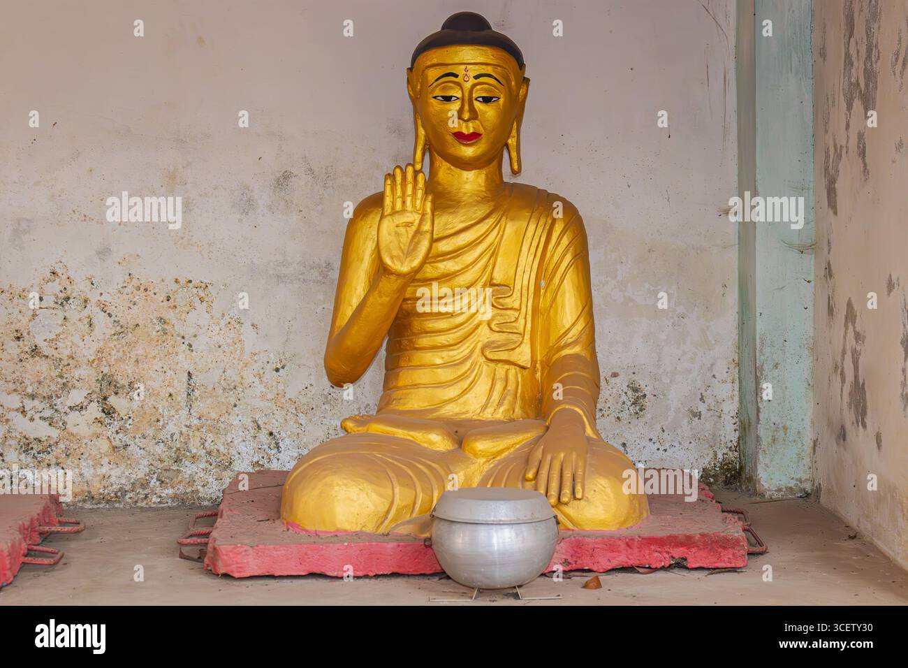 Magnifica statua dorata del Buddha con gesti di benedizione delle mani sullo sfondo delle antiche mura del tempio Foto Stock