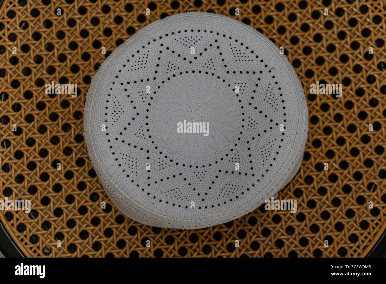 Elegante cappellino di preghiera ricamato bianco posto ordinatamente su una sedia in canna intrecciata Foto Stock