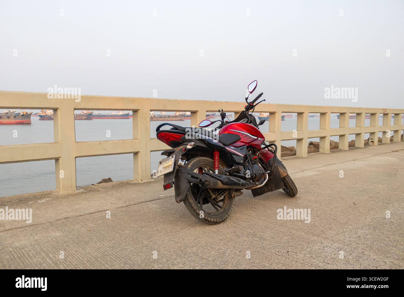 Bici rossa solitaria che poggia su un'ampia strada costiera accanto alla tranquilla baia del Bengala in Bangladesh Foto Stock