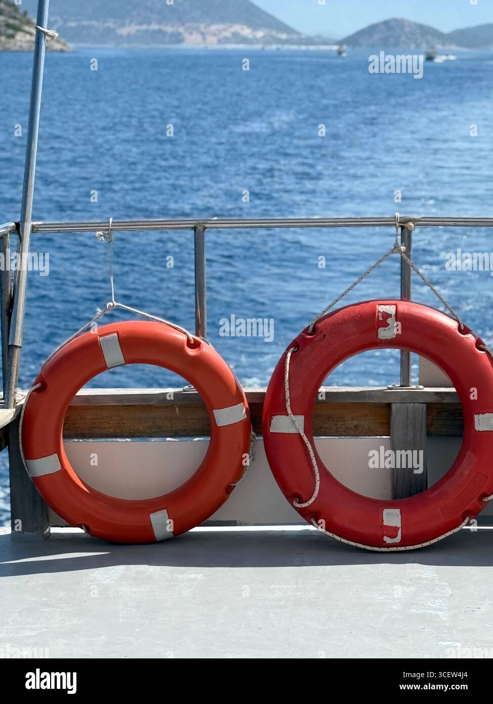 Due luminose cinture di salvataggio appese sul lato di una barca turistica con il mare blu sullo sfondo, che simboleggiano la sicurezza e il viaggio - Immagine stock catturata con smartphone