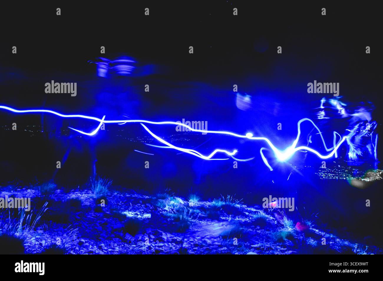 Foto a lunga esposizione che mostra una pista luminosa blu attraverso un paesaggio roccioso notturno con figure umane spettrali. Foto Stock