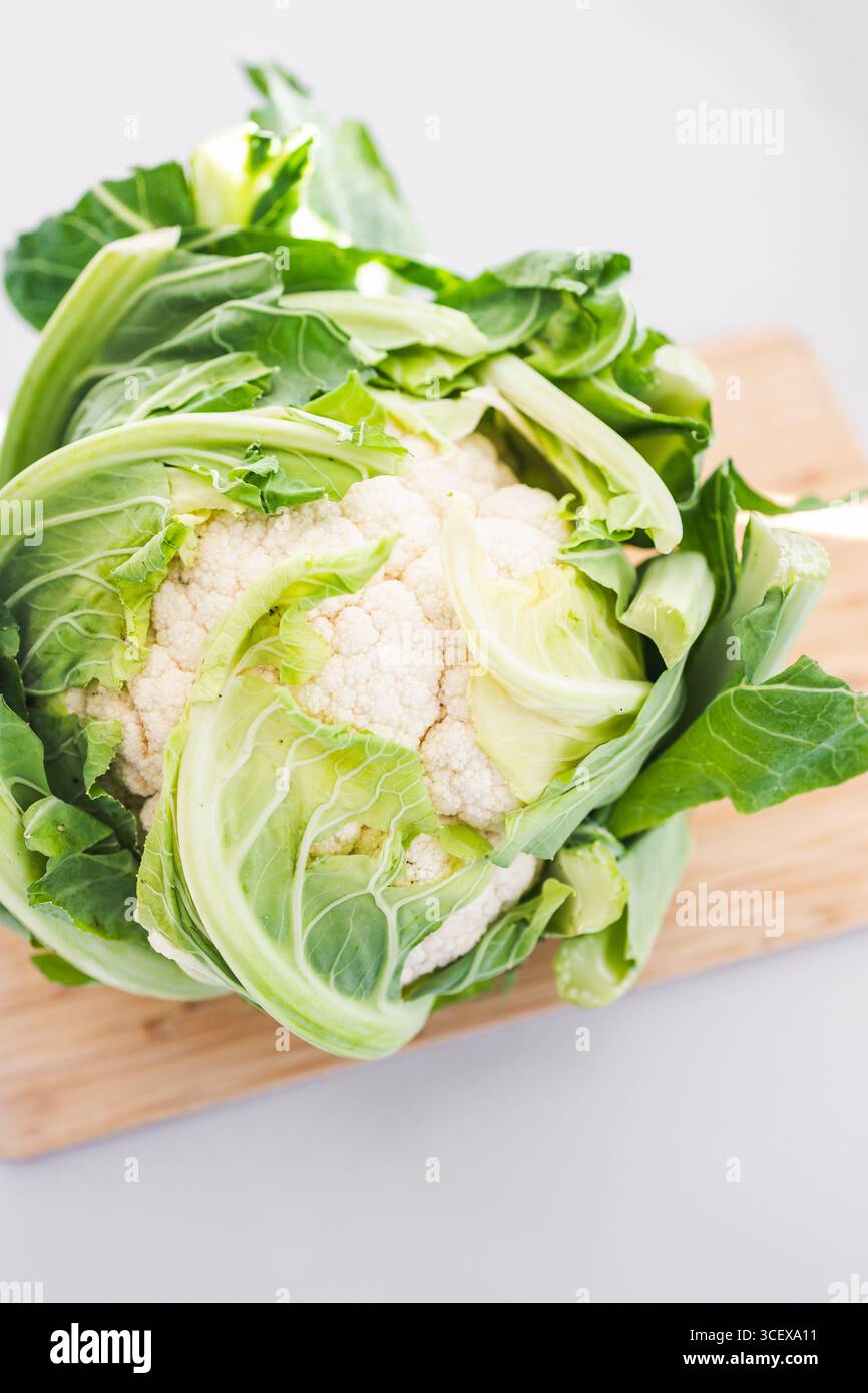 testa intera di cavolfiore con foglie su tagliere in legno sul banco cucina tema ricette salutari, prediabete e pasti diabetici-friendly Foto Stock testa intera di cavolfiore con foglie su tagliere in legno sul banco cucina tema ricette salutari, prediabete e pasti diabetici-friendly Foto Stock