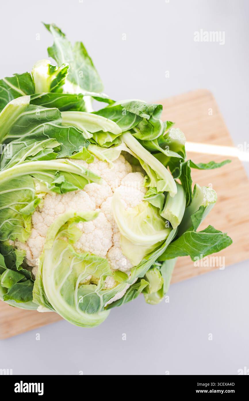 testa intera di cavolfiore con foglie su tagliere in legno sul banco cucina tema ricette salutari, prediabete e pasti diabetici-friendly Foto Stock testa intera di cavolfiore con foglie su tagliere in legno sul banco cucina tema ricette salutari, prediabete e pasti diabetici-friendly Foto Stock