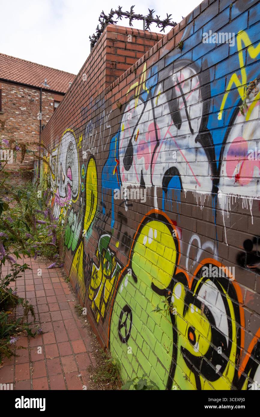 Graffiti Street art che coprono una parete in mattoni rossi con colori audaci, cartelli e vernice spray in un ambiente urbano Foto Stock