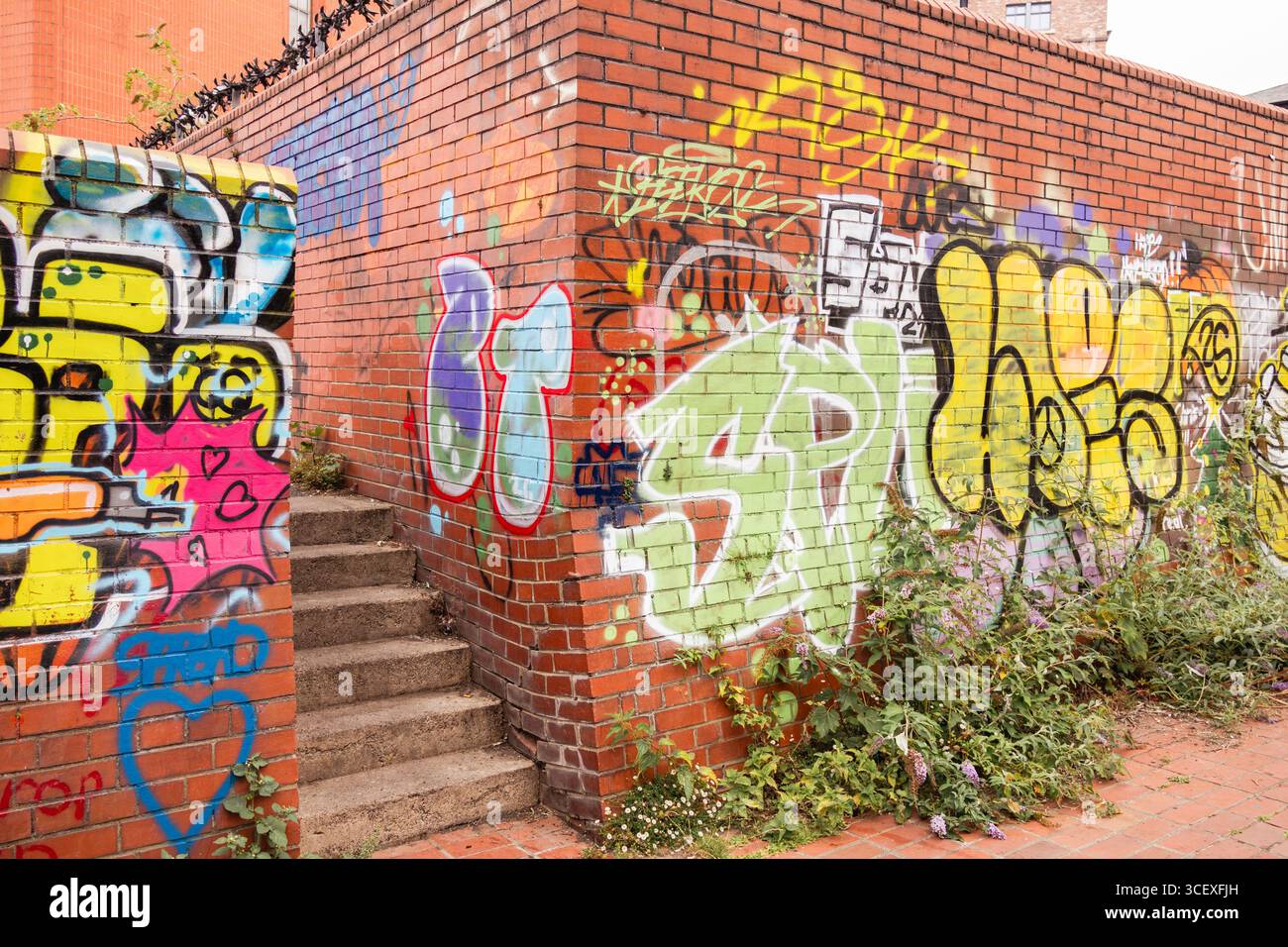 Graffiti Street art che coprono una parete in mattoni rossi con colori audaci, cartelli e vernice spray in un ambiente urbano Foto Stock