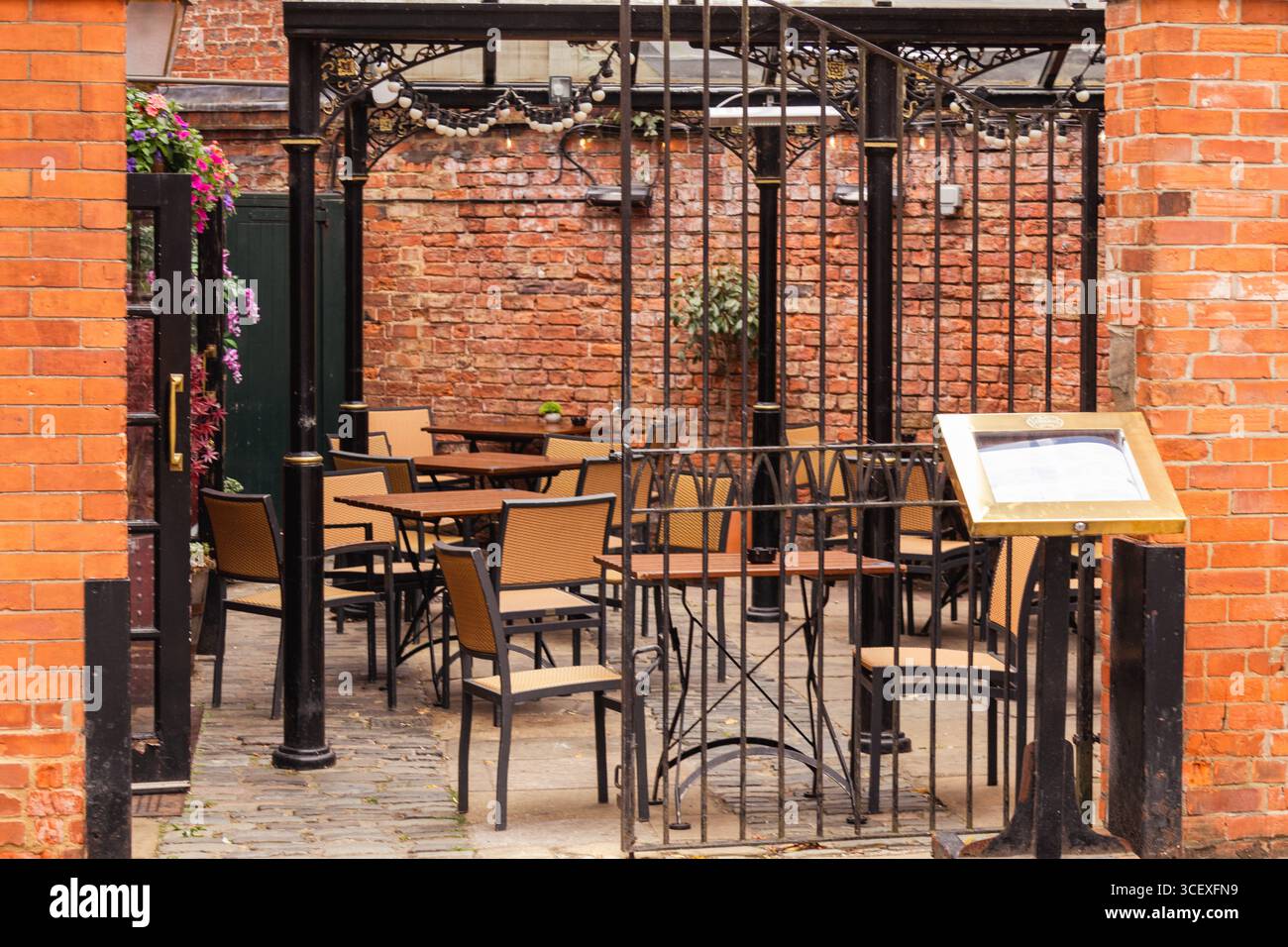 Incantevole caffetteria all'aperto con tavoli e sedie circondata da pareti in mattoni e un cancello decorativo in ferro battuto, perfetta per l'ospitalità e l'ospitalità Foto Stock