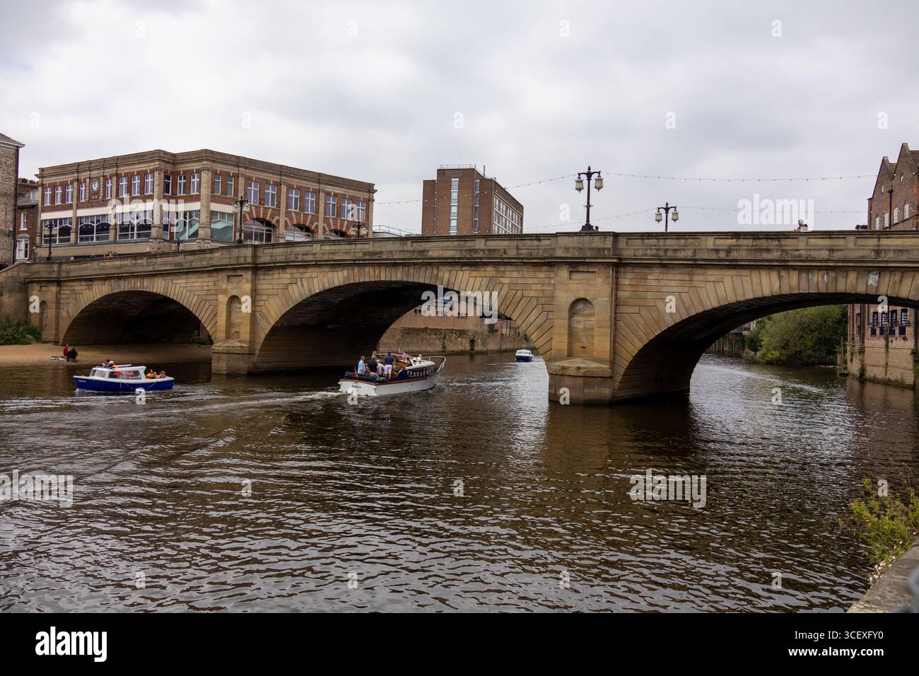 Storico ponte ad arco in pietra che attraversa un fiume della città con barche che passano sotto, circondato da edifici urbani sotto cieli nuvolosi Foto Stock