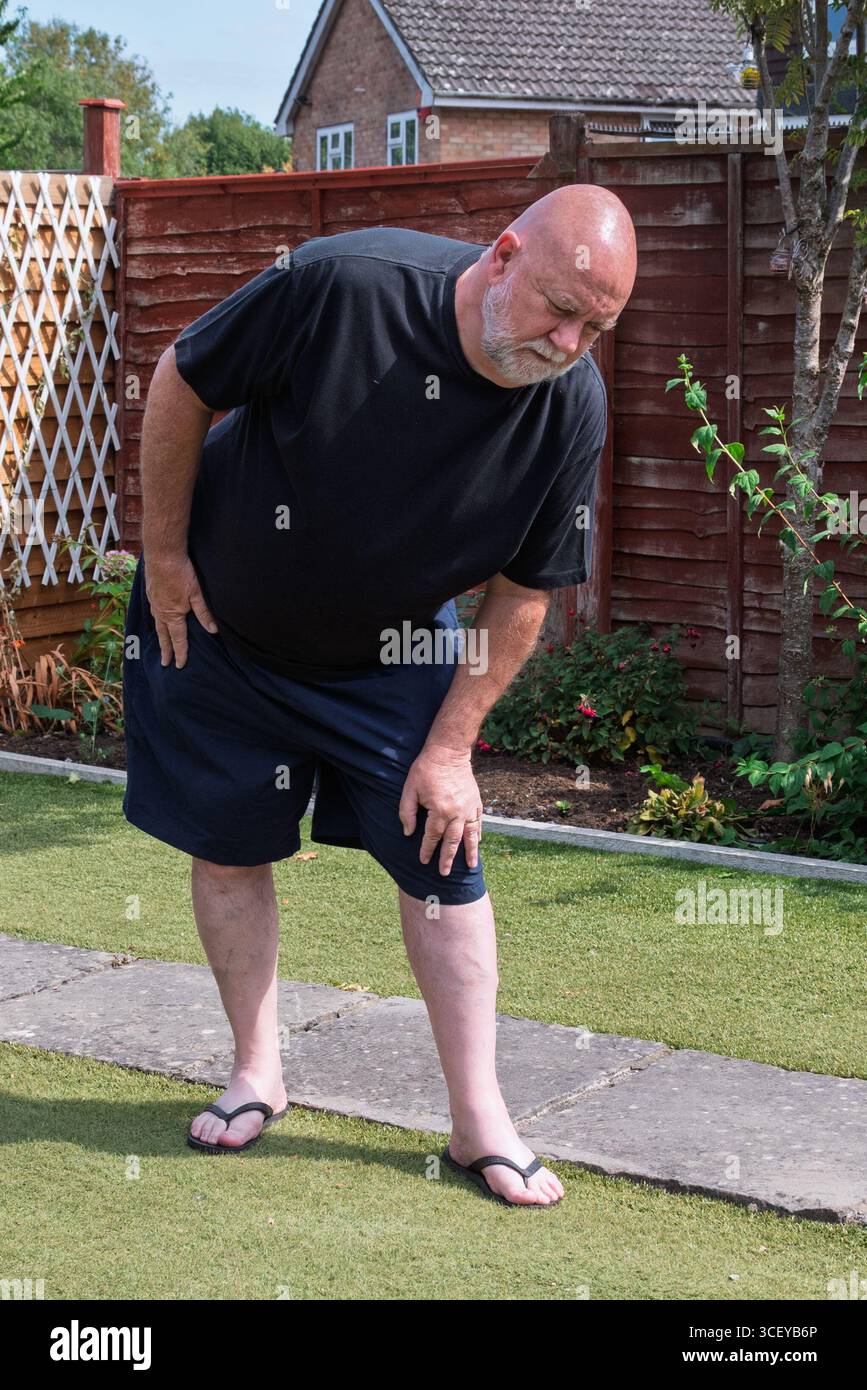 Uomo che soffre di dolore al ginocchio in giardino. Uomo anziano con dolori articolari. Foto Stock