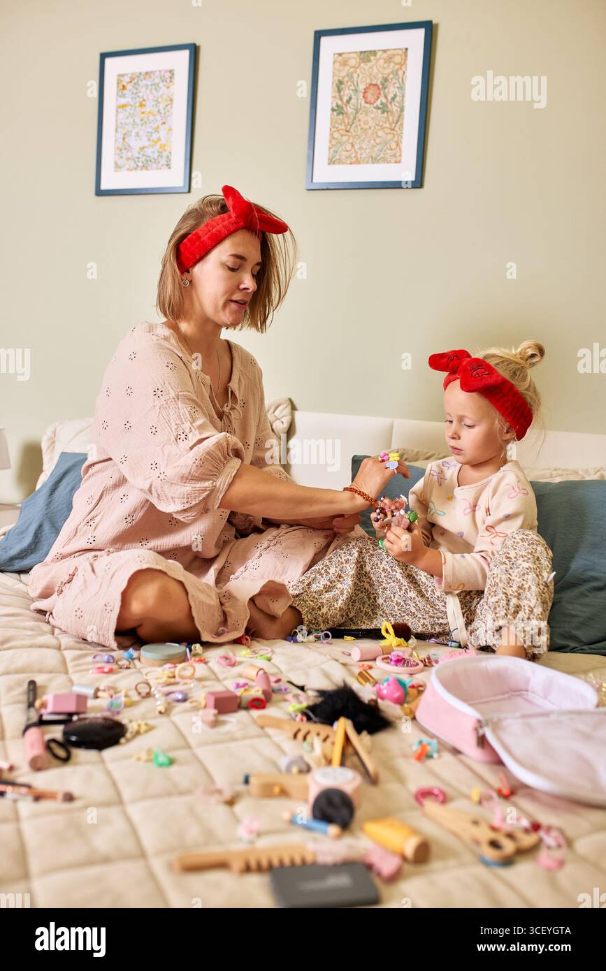 Una madre amorevole passa del tempo di qualità legandosi con la sua giovane figlia. Si divertono a giocare con oggetti per il trucco e vari accessori colorati, creando c Foto Stock