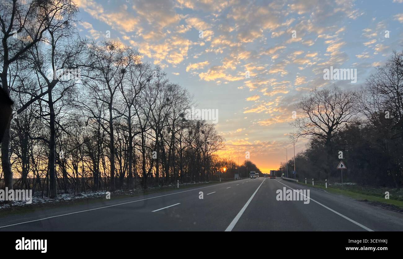 un dolce tramonto dorato davanti alla strada, ai campi e un viaggio sulla strada Foto Stock