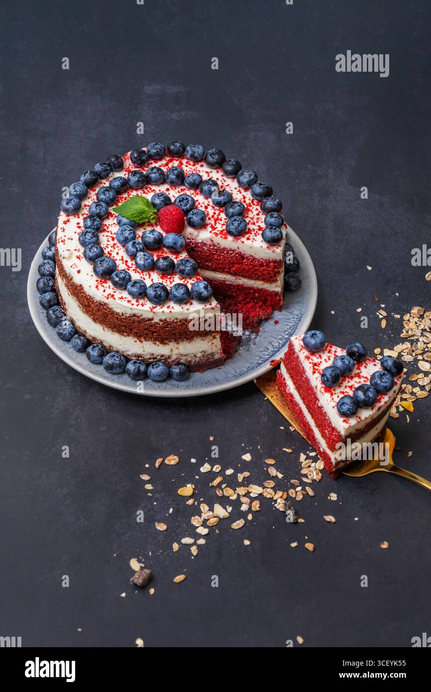 Boutique Red Velvet Cake: Decorazione minimalista con mirtilli selvatici e petali di rosa commestibili su una glassa impeccabile Foto Stock