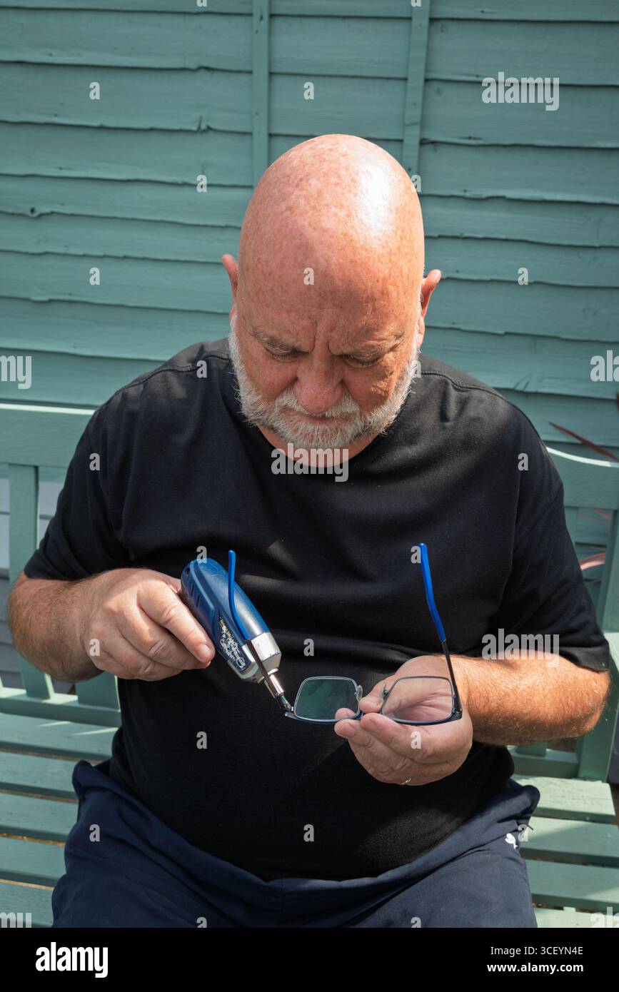 Uomo che ripara gli occhiali con un piccolo cacciavite. Riparazione di occhiali fai da te. Vecchio con il caffè sullo smartphone. uomo anziano e tecnologia in uso Foto Stock
