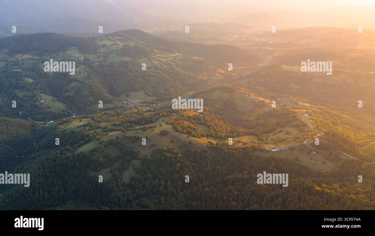 Il morbido crepuscolo scende su un terreno coperto da foresta, avvolgendo il paesaggio rurale in una calmante foschia estiva Foto Stock