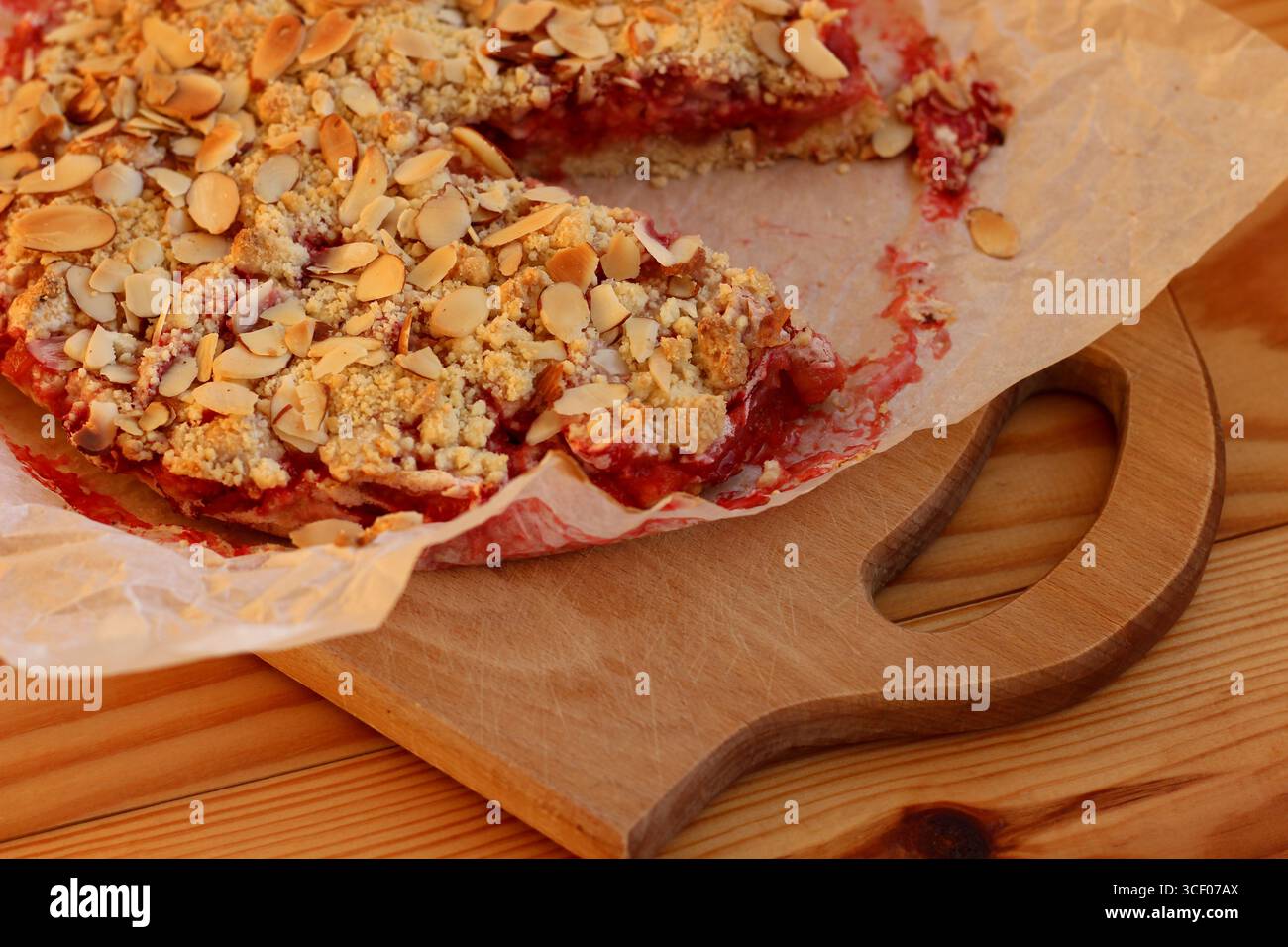 Torta sbriciolata di fragole e mandorle appena sfornata con condimento croccante su carta pergamena. All'interno succoso, dorato e rustico all'esterno Foto Stock