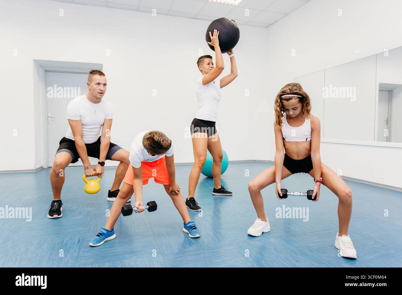 Sessione di allenamento in famiglia in palestra con pesi e attrezzature fitness, promuovendo la salute, la forza e la solidarietà attraverso l'esercizio fisico. Foto Stock