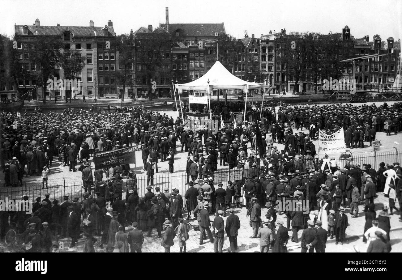Questa foto del 1920 mostra la celebrazione del primo maggio del Partito Comunista a Parkschouwburg, Amsterdam. La folla si riunisce intorno a una tenda aperta, con case sui canali e un ponte levatoio visibili sullo sfondo. Uno degli striscioni recita "contro la legge soffocante di Heemskerk!” Foto Stock