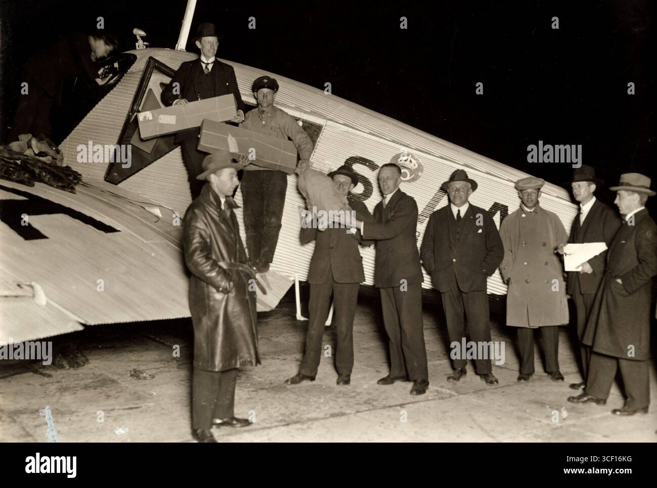Questa foto del 1928 mostra un gruppo di dieci uomini in piedi accanto a un aereo del servizio postale notturno all'aeroporto di Schiphol. Alcuni trasportano pacchi postali e una borsa postale, che riflettono l'aviazione e le operazioni postali nei Paesi Bassi all'inizio del XX secolo. Foto Stock
