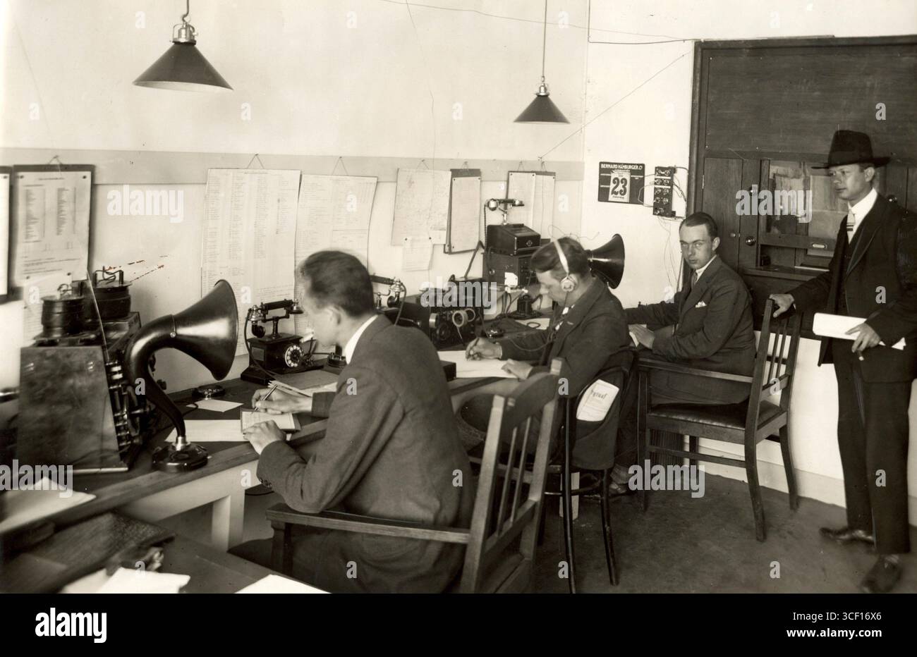 Nel 1928, tre lavoratori del servizio radio di Schiphol sono visti al lavoro, uno indossava una cuffia e un altro registrava i dati. L'immagine mette in evidenza le prime tecnologie di comunicazione aeronautica nei Paesi Bassi. Foto Stock