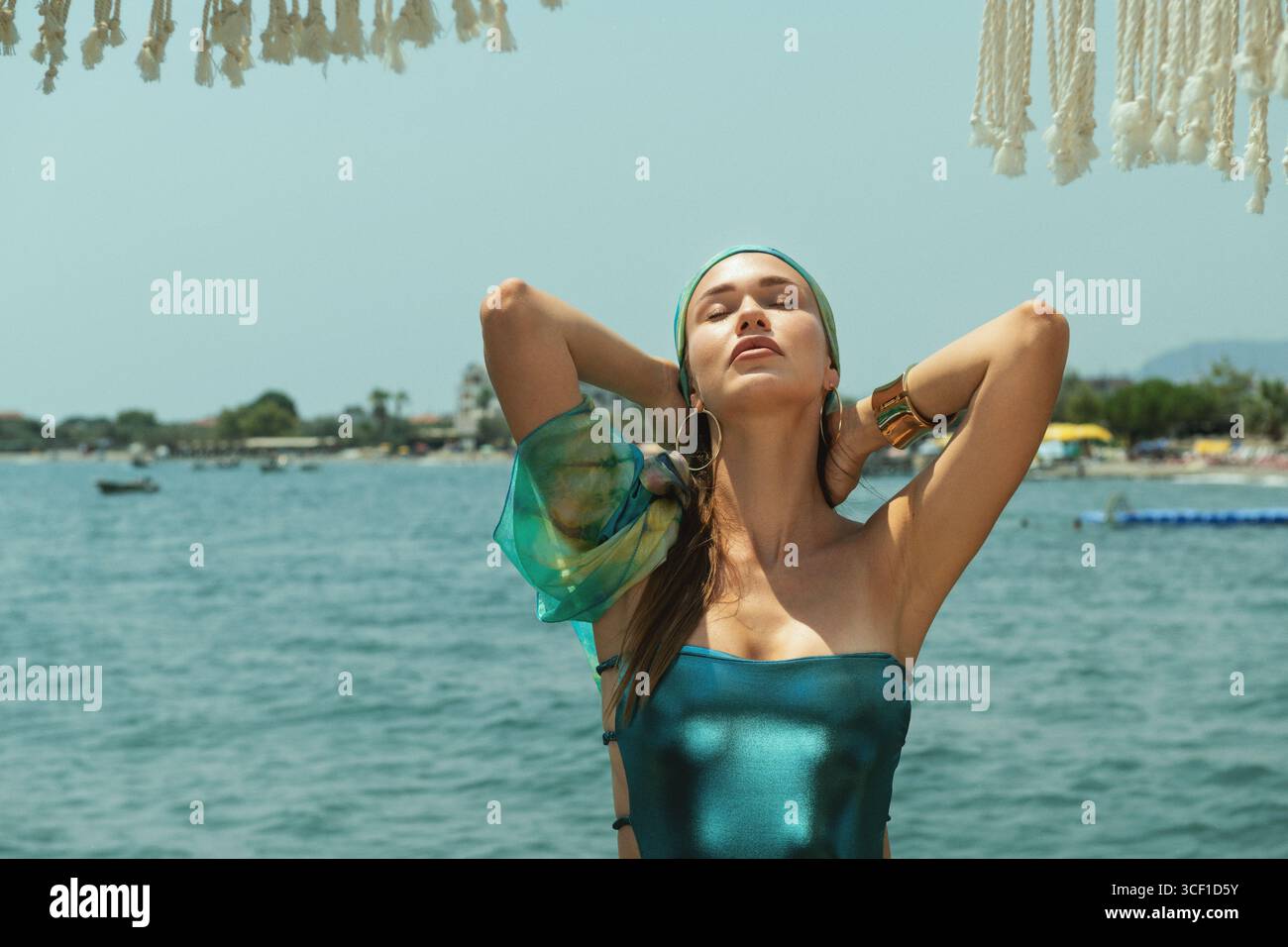 Attraente bionda dagli occhi blu che indossa bikini blu e bandana abbinata che posa in sicurezza vicino all'oceano Foto Stock