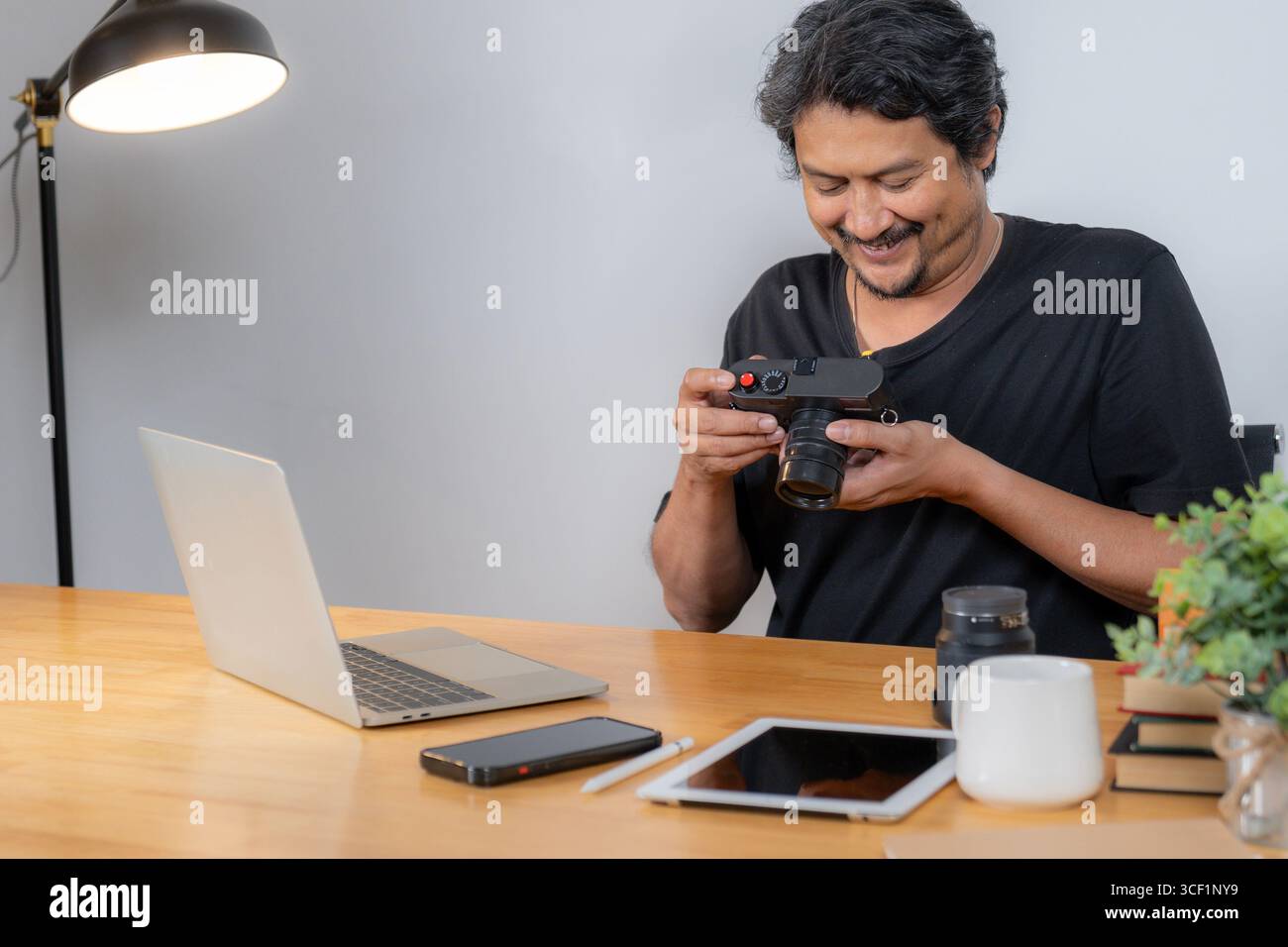 Un giovane fotografo maschile che lavora da casa, che modifica le foto su un computer con software creativo in un ambiente accogliente Foto Stock