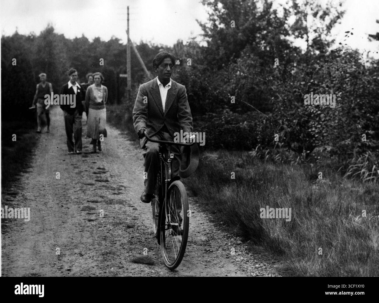 Insegnante spirituale indiano Jiddu Krishnamurti (1895-1986) in bicicletta, seguito da alcuni individui (possibilmente studenti o seguaci), a Ommen, Paesi Bassi, 1929. Foto Stock