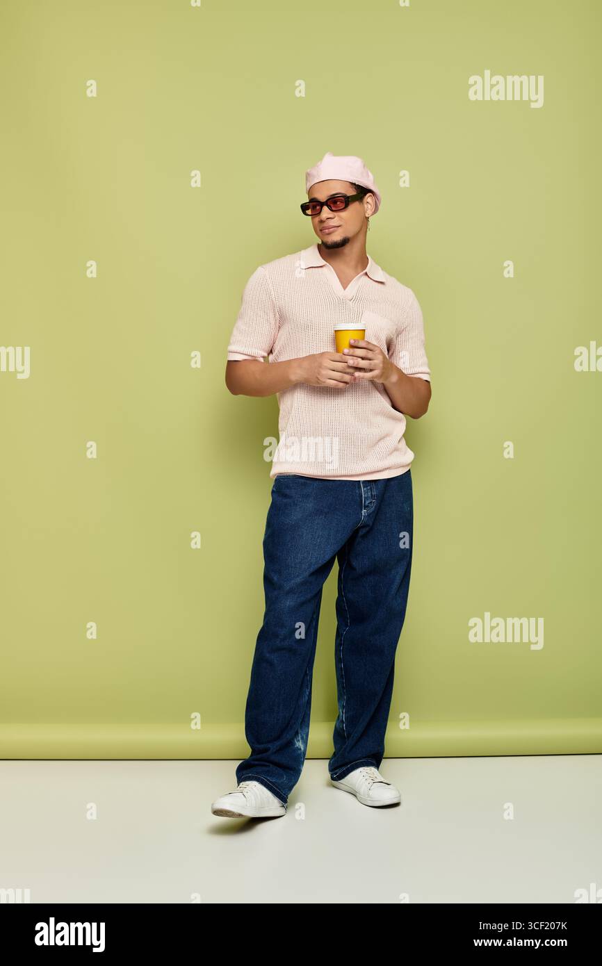 Un giovane uomo nero alla moda posa con sicurezza con un drink in mano. Foto Stock