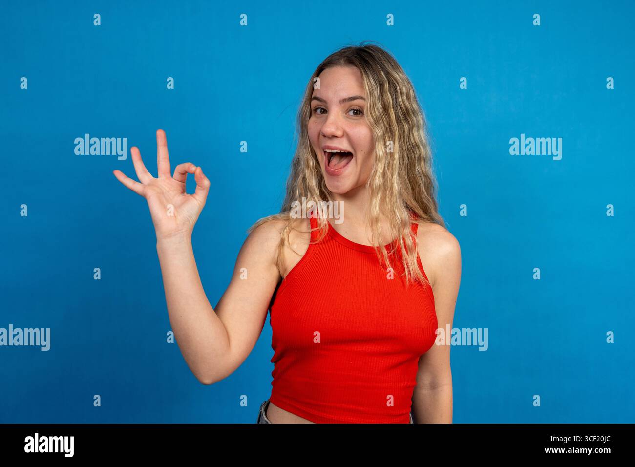 Ritratto di una giovane donna allegra che fa gesto ok su uno sfondo blu vibrante Foto Stock