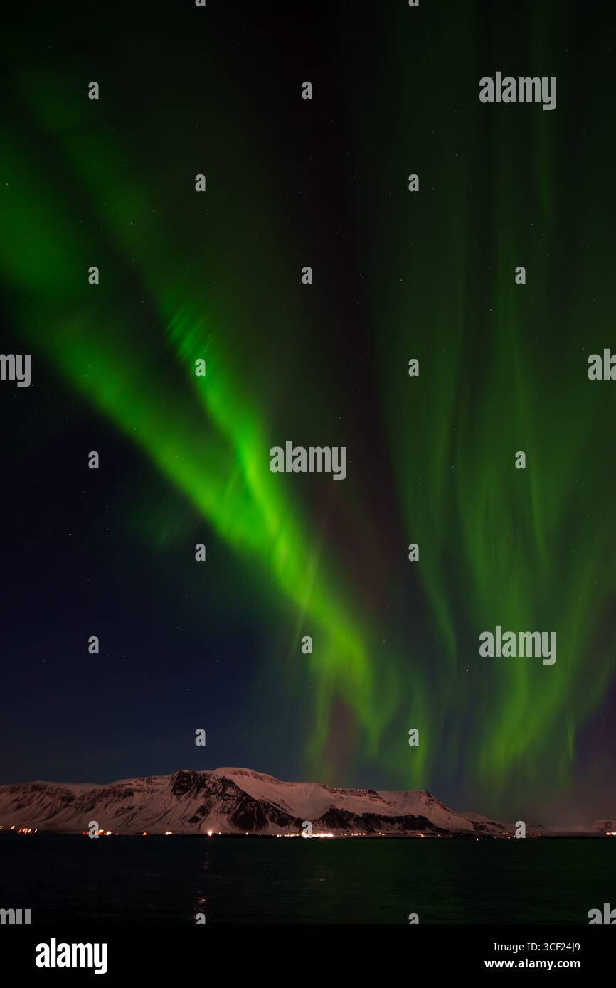 Raggi di aurora verde che si innalzano sopra una silhouette di montagna scura, Islanda Foto Stock