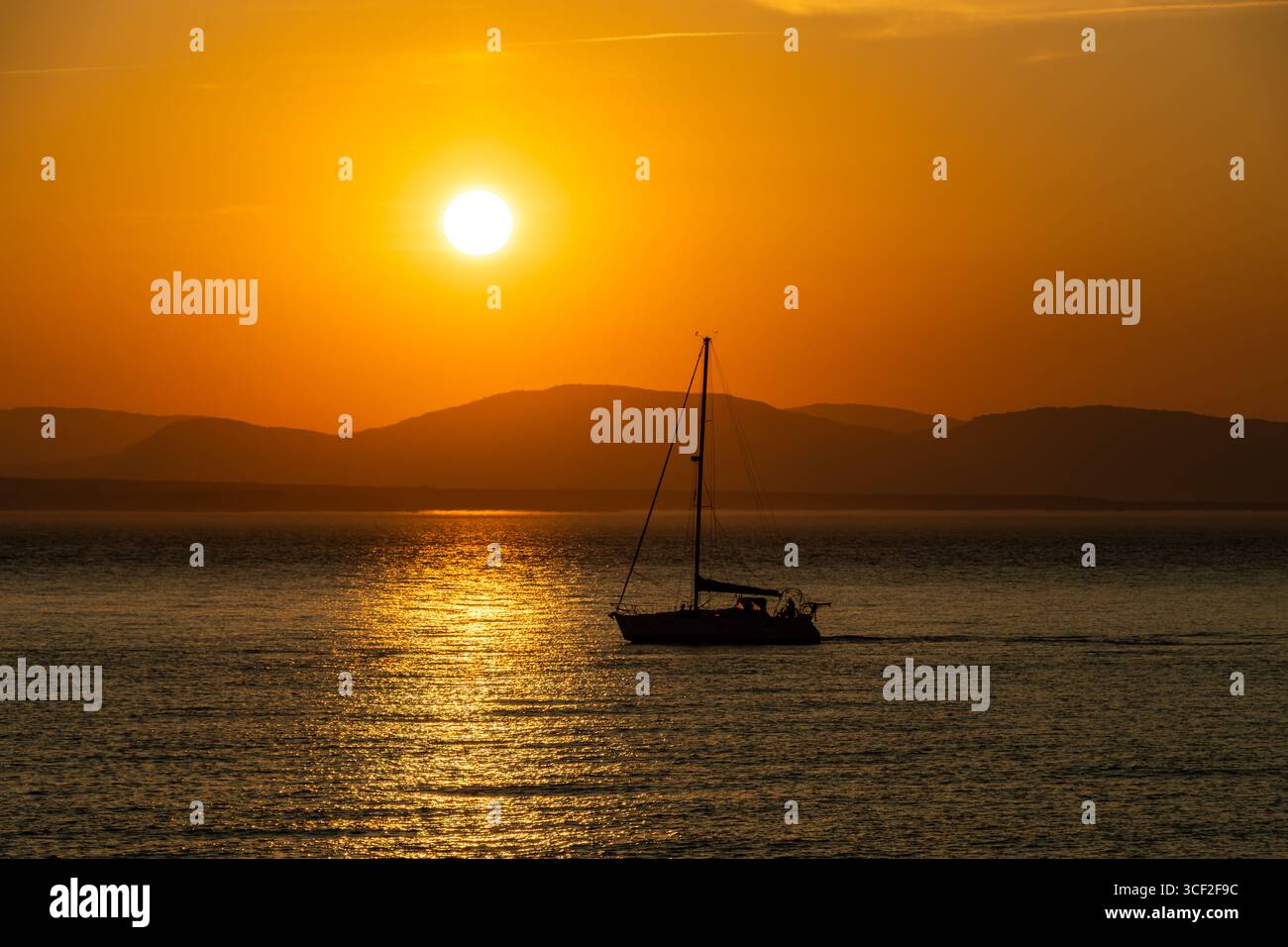 Silhouette di una barca a vela sul fiume San Lorenzo di fronte a Riviere-du-Loup al tramonto in agosto. Colore arancione dominato. Foto Stock