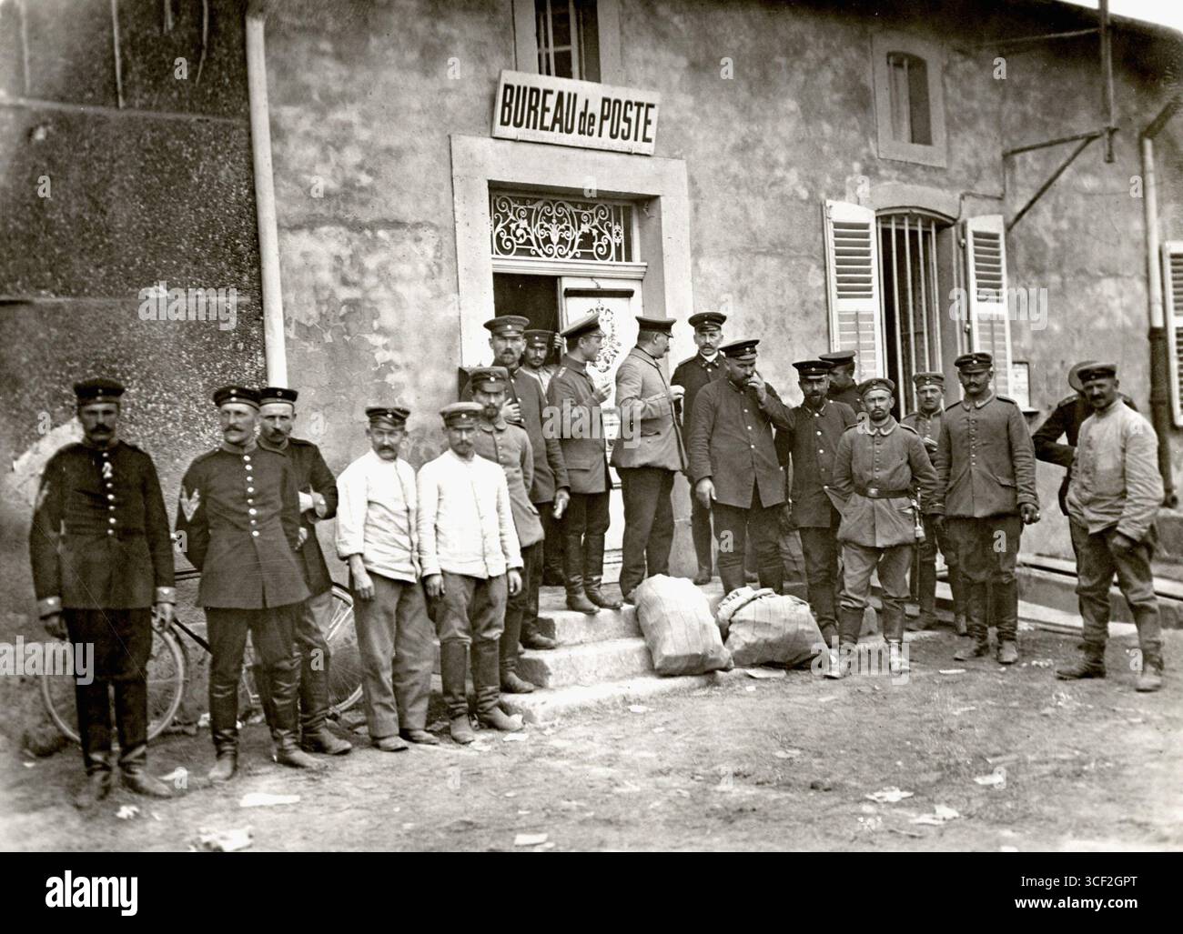 Nel 1914, durante la prima guerra mondiale, diciannove uomini tedeschi assunsero le funzioni di operai postali francesi nel villaggio di Jonville, in Francia. Sono di fronte a un ufficio postale con le uniformi militari. Foto Stock