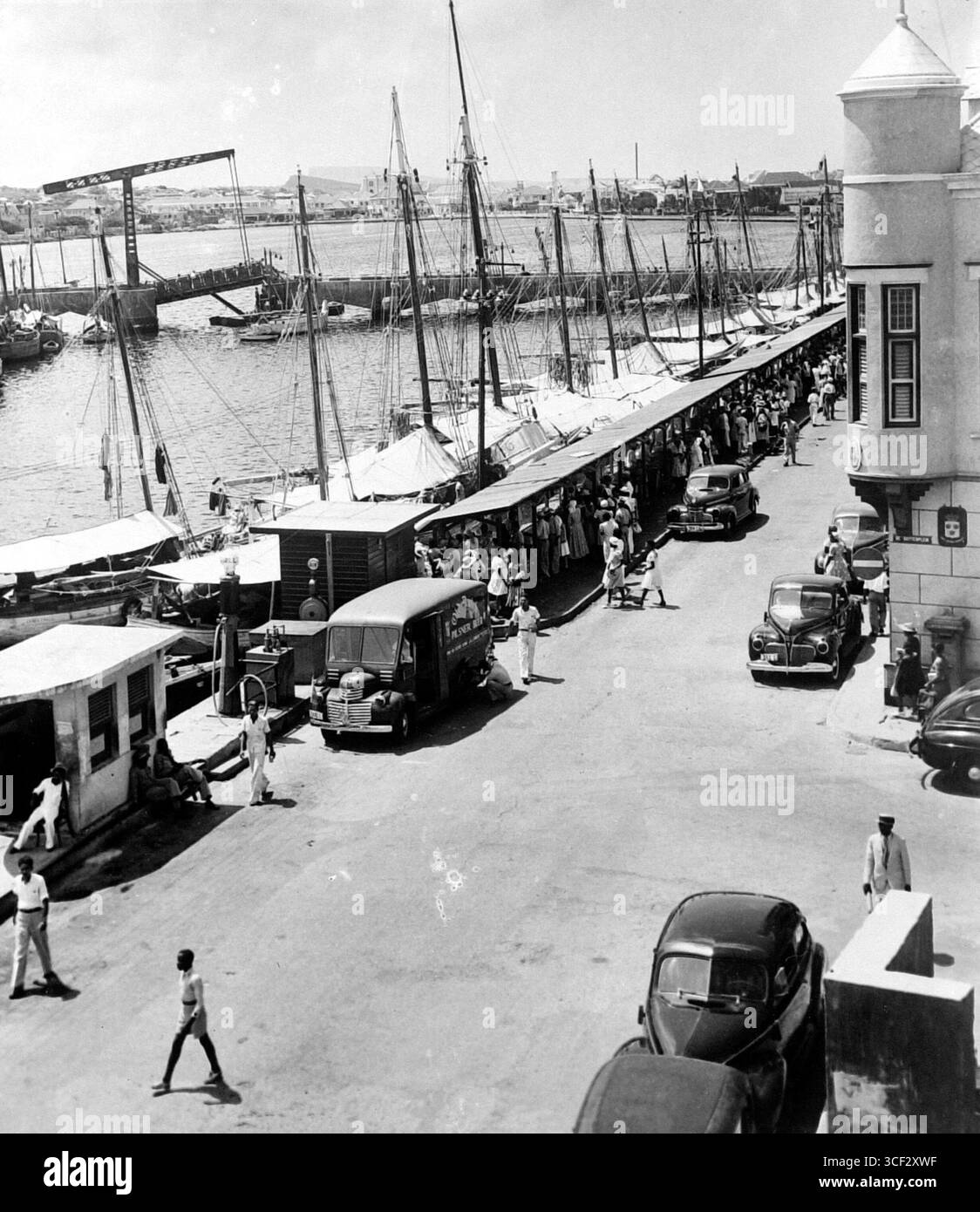 Questa fotografia del 1947 offre una vista del mercato di De Ruyterkade, con bancarelle di verdure accanto alle barche che hanno consegnato le merci. L'immagine cattura anche una stazione di servizio Shell e un ponte aperto, fornendo un'istantanea della vita urbana nei Paesi Bassi del dopoguerra. Foto Stock