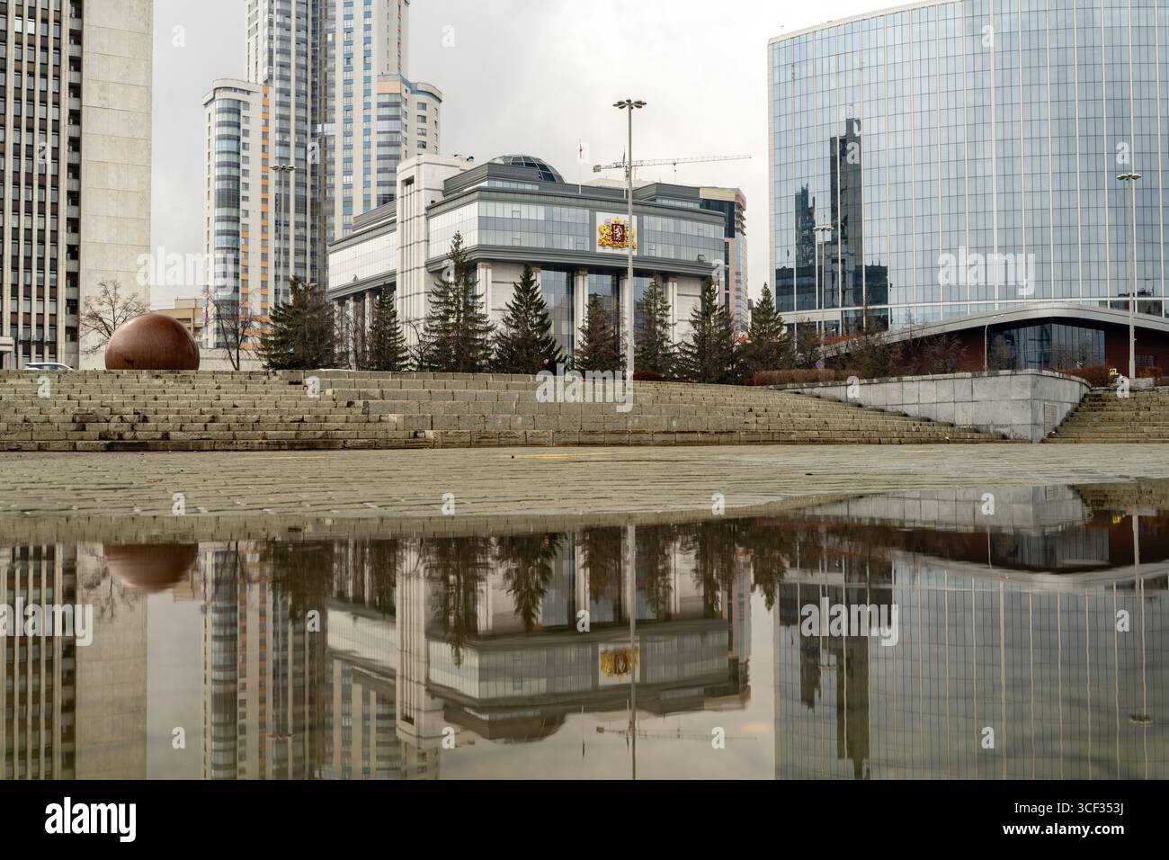 Edificio governativo a Ekaterinburg, in Russia, con una facciata moderna, bandiere nazionali e lo stemma regionale. Alberi invernali e gradini di pietra nel Foto Stock