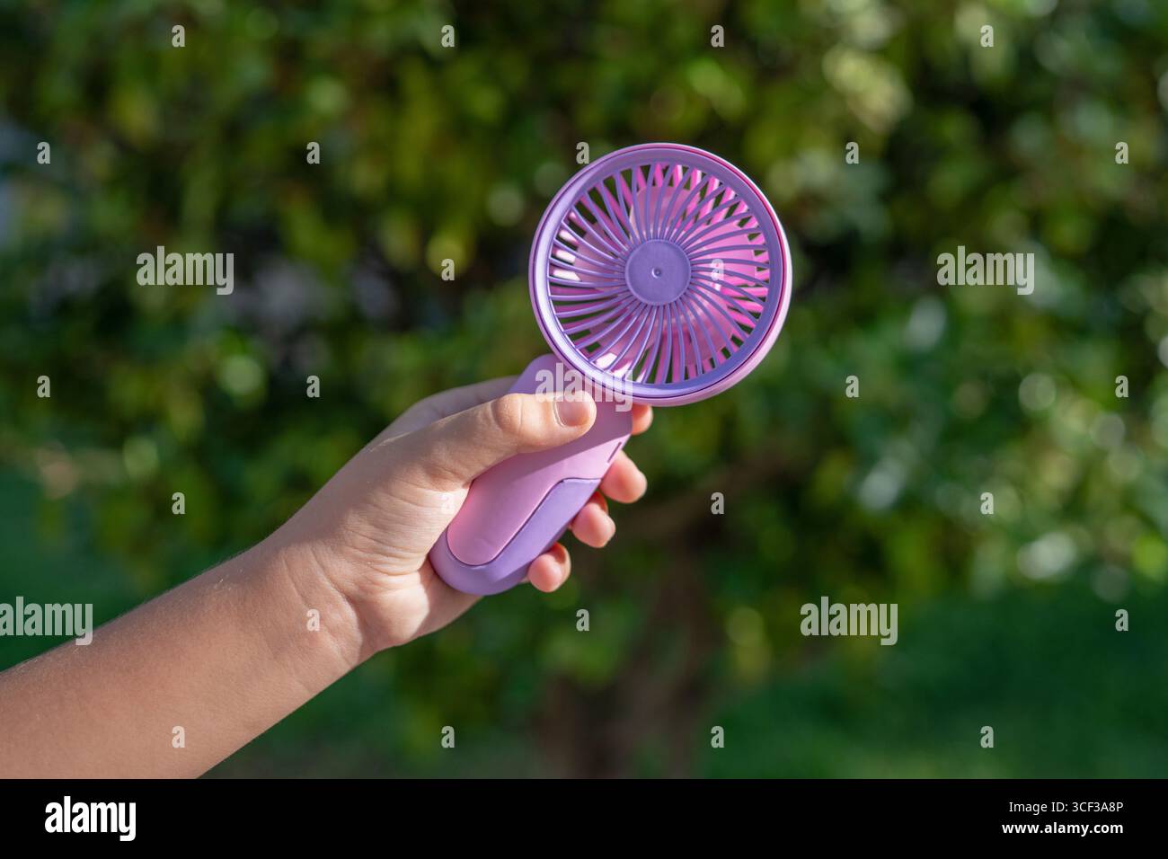 Tenere a mano il mini ventilatore portatile all'aperto alla luce del sole Foto Stock