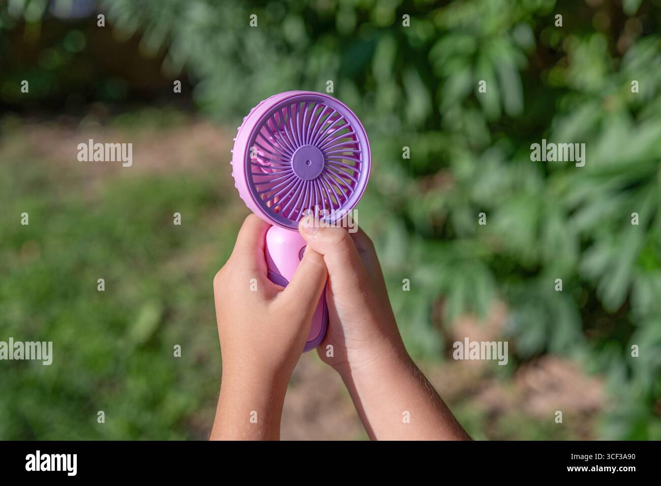 Tenere a mano il mini ventilatore portatile all'aperto alla luce del sole Foto Stock
