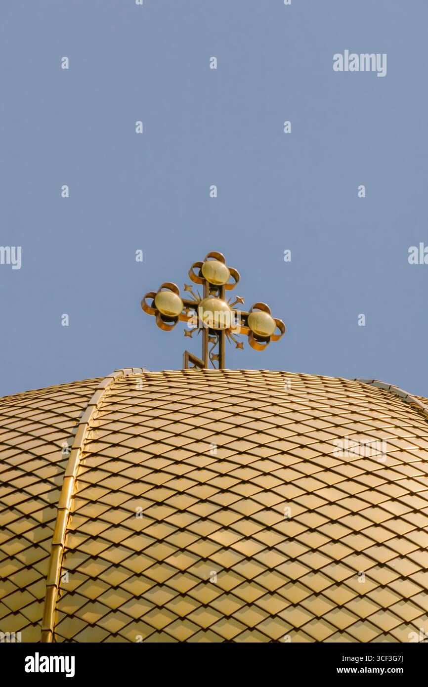 Una suggestiva cupola dorata sormontata da una croce si erge maestosamente contro un cielo blu vibrante. La luce del sole mette in risalto gli intricati dettagli della cupola, refle Foto Stock