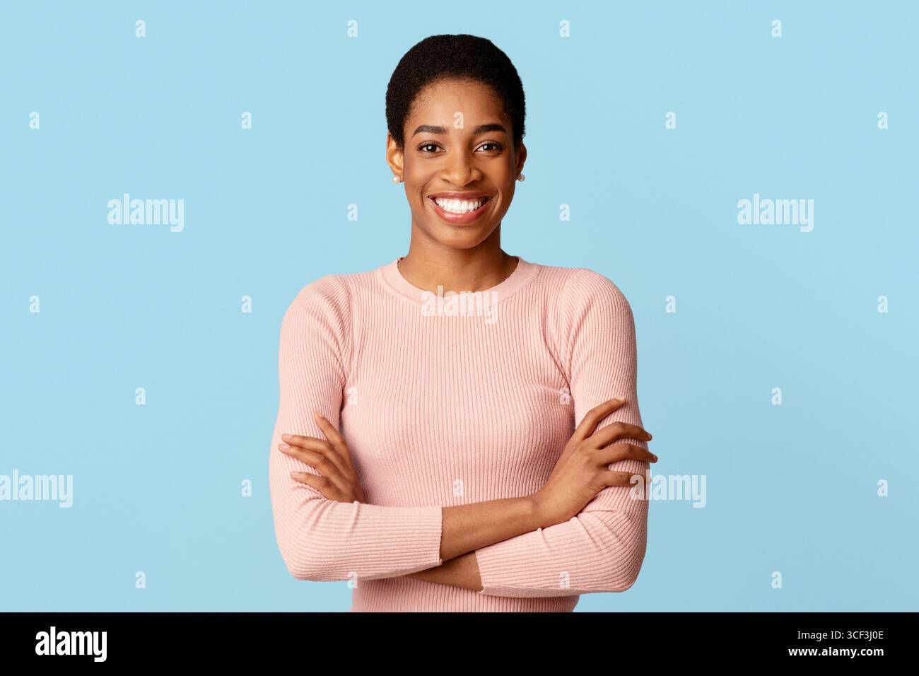 Ritratto di donna nera positiva in posa con braccia ripiegate su sfondo blu Foto Stock