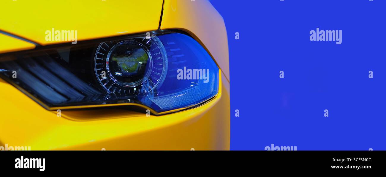 Primo piano faro anteriore con luce allo xeno su una vettura sportiva gialla su sfondo blu, spazio copia Foto Stock