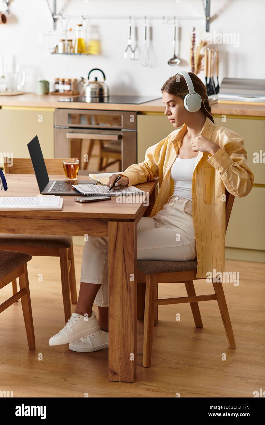 Concentrata sul suo lavoro, una giovane donna siede comodamente nella sua luminosa cucina, immersa nell'apprendimento. Foto Stock
