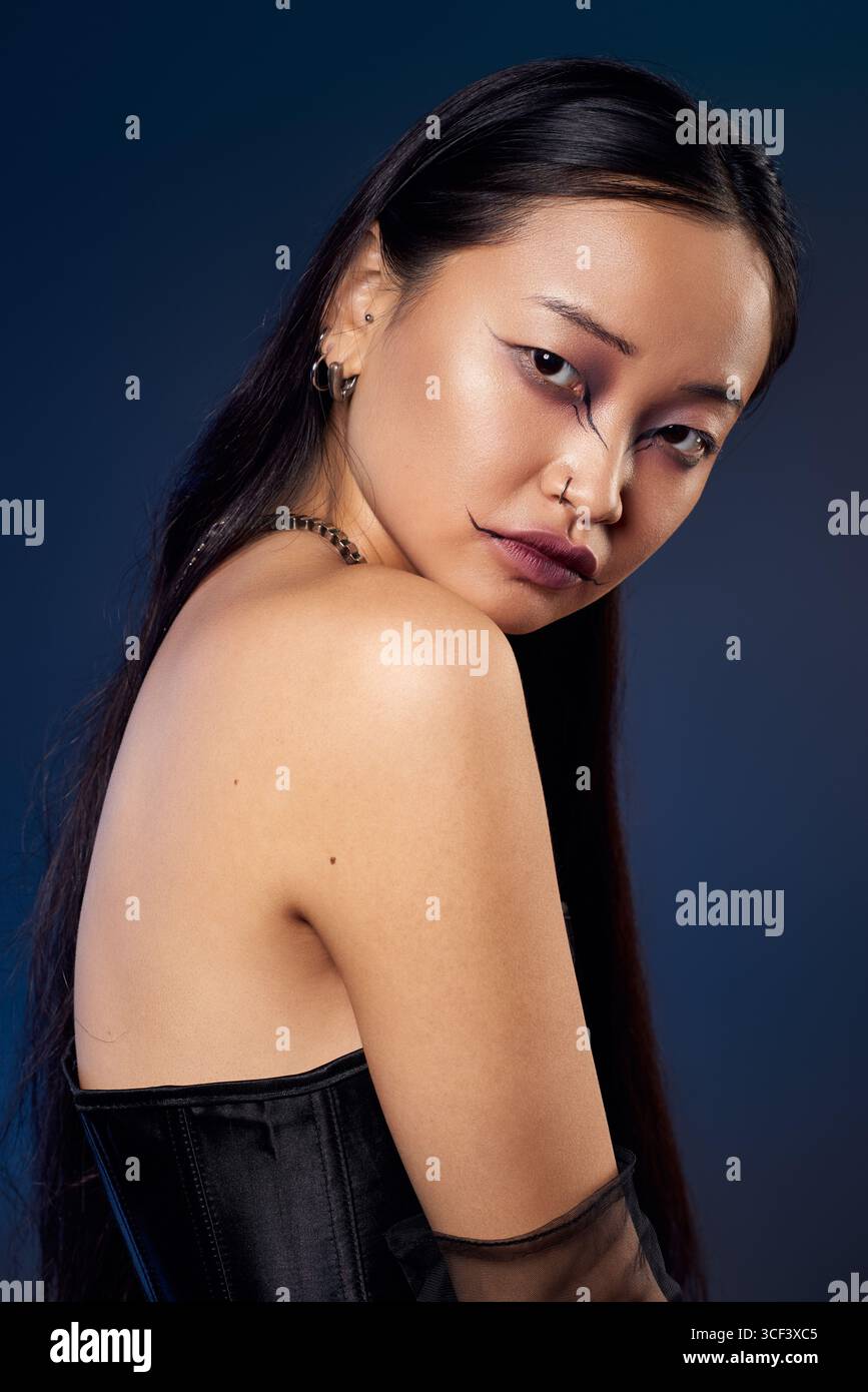 Un ritratto creativo di una giovane donna in un corsetto nero che mostra un trucco spettrale su uno sfondo blu. Foto Stock