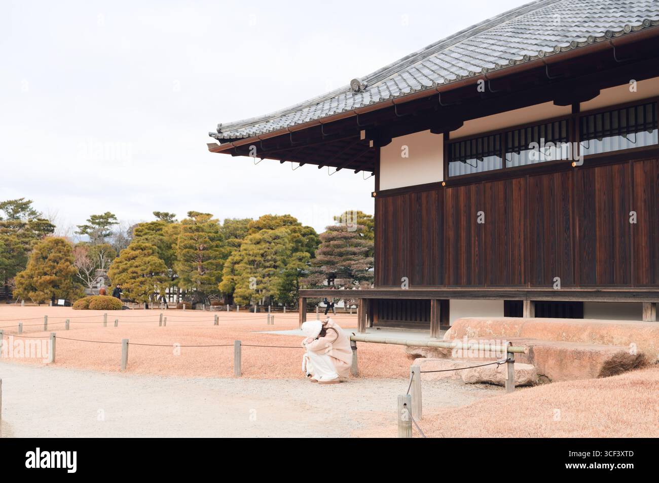Una figura vestita di bianco siede arricciata dalle sale in legno del Castello Nijo, circondato da tranquilli giardini e dal silenzio invernale Foto Stock
