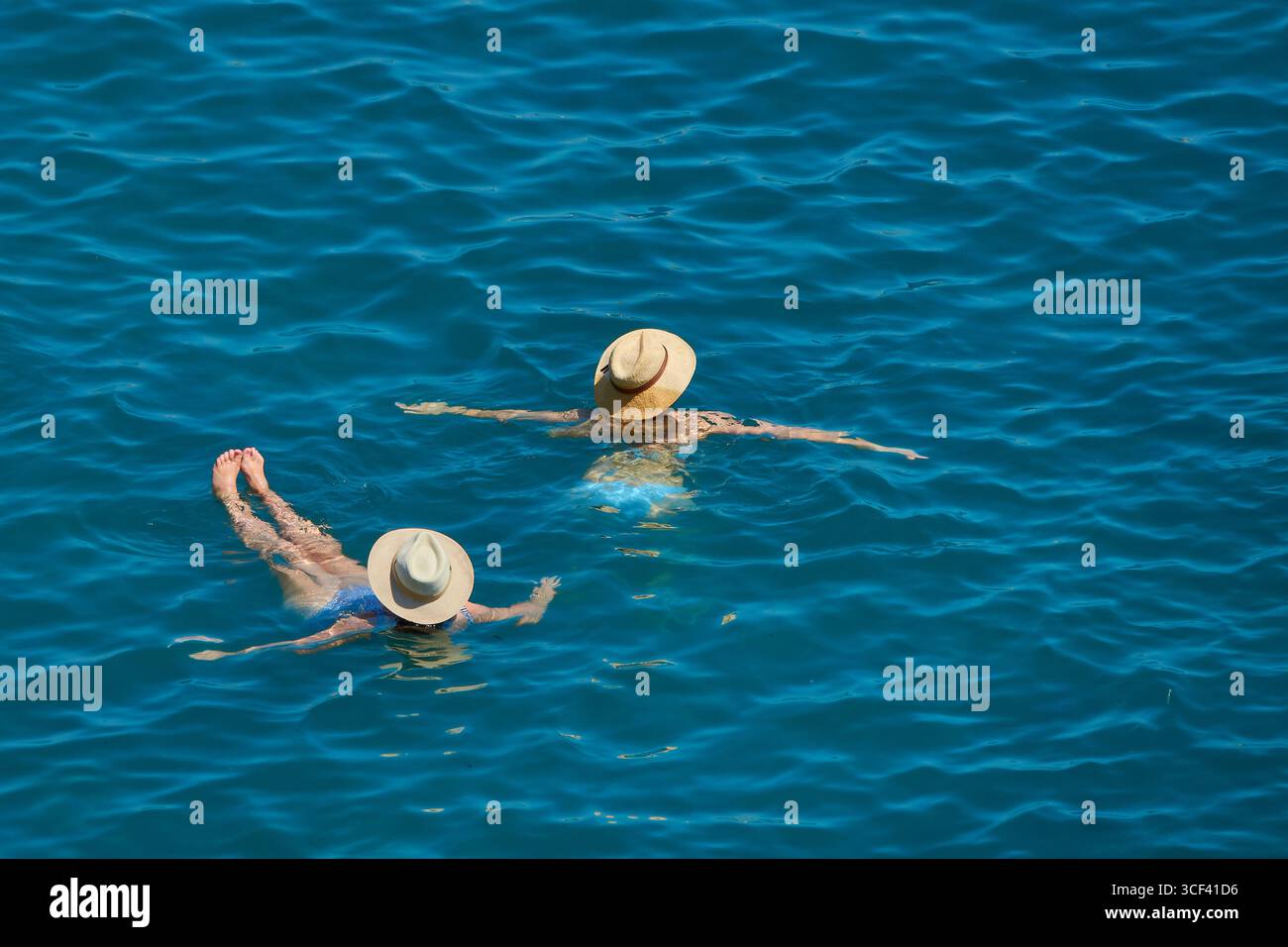 Due donne che si rilassano nell'acqua blu brillante indossando cappelli di paglia Foto Stock