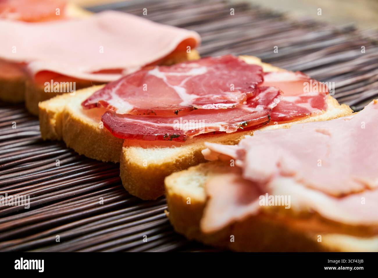 Fette di pane con affettati assortiti su un tappeto intrecciato, in primo piano per evidenziare texture e colori. Ideale per il cibo o per contenuti editoriali. Foto Stock