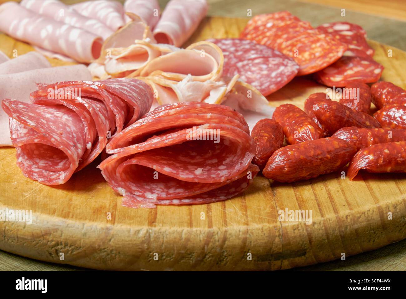 Tavola di legno con una varietà di salumi: salumi, prosciutti e salsicce disposti con stile. Texture e colori si distinguono in una presentazione ideale per Foto Stock