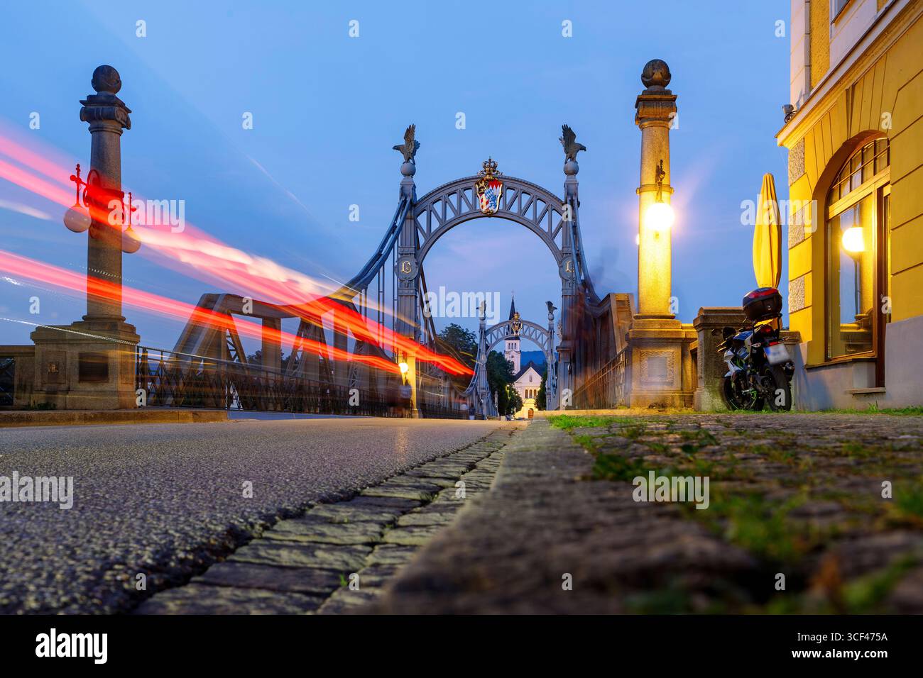Ponte di campagna di Laufen an der Salzach in Berchtesgadener Land in alta Baviera, Baviera, Germania con vista sulla chiesa parrocchiale di San Nicola a Oberndorf vicino a Salisburgo, Salisburgo, Austria alla luce della sera con striscia luminosa rossa Foto Stock